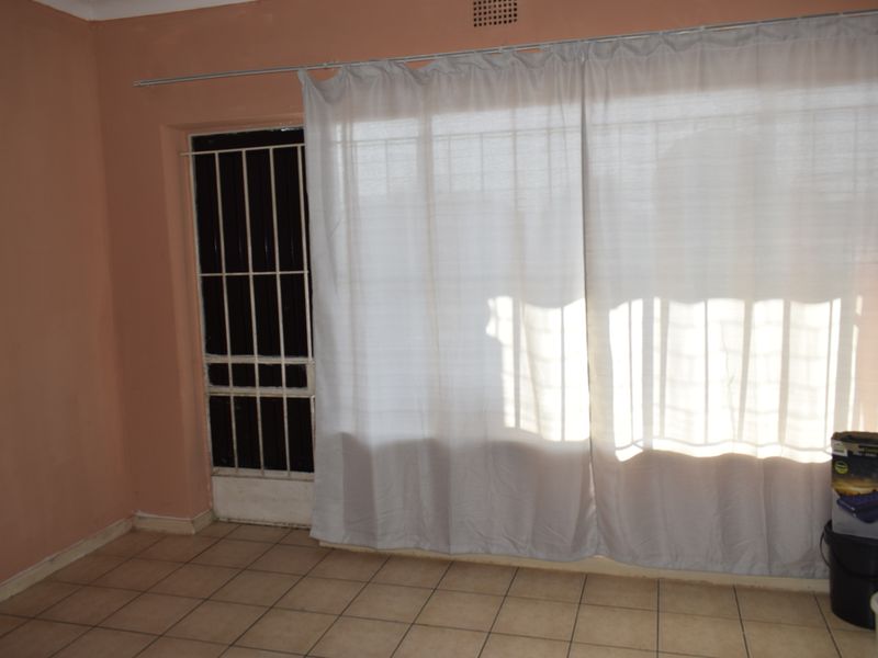 An empty living area featuring tiled flooring, a security gate, and a curtain rail, providing a blank canvas for potential interior design updates.