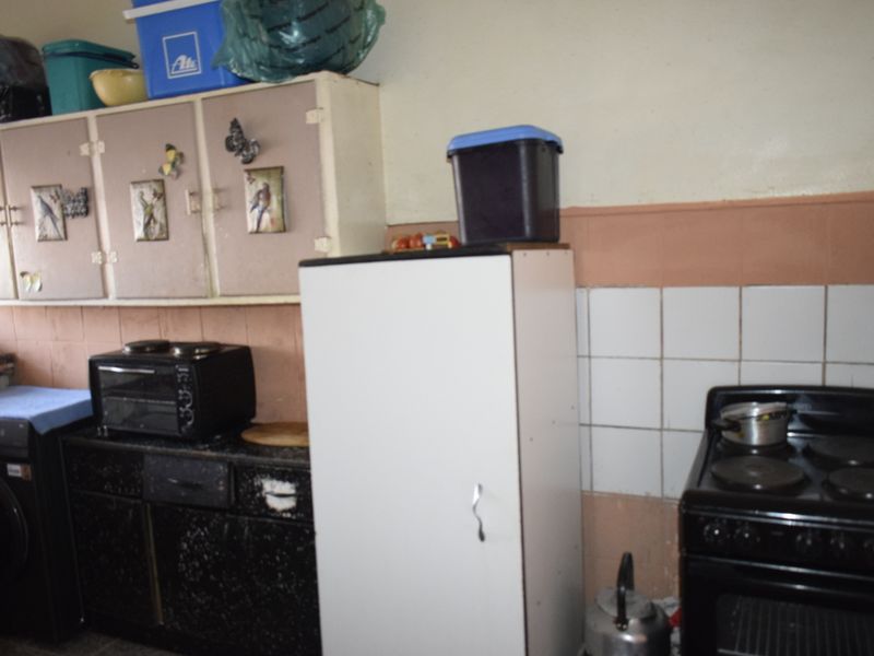 A dated kitchen area featuring built-in cabinetry, a tiled splashback, and a freestanding stove, requiring cosmetic updates to modernize the space.