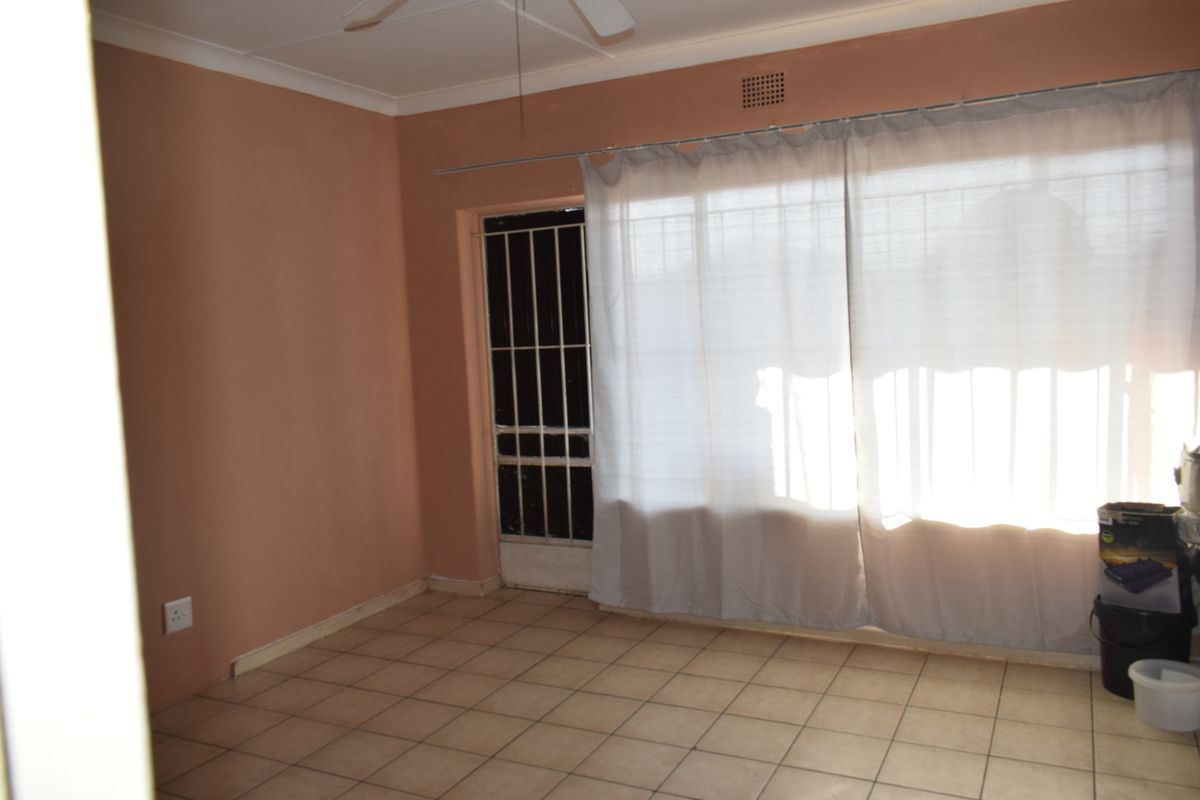 An empty living room featuring tiled flooring, a ceiling fan, and a sliding door with an integrated security gate.