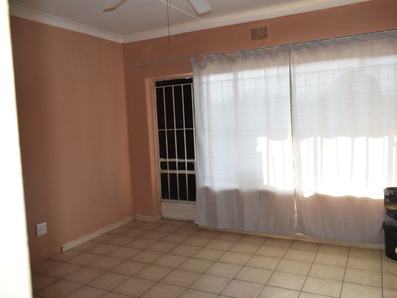 An empty living room featuring tiled flooring, a ceiling fan, and a sliding door with an integrated security gate.
