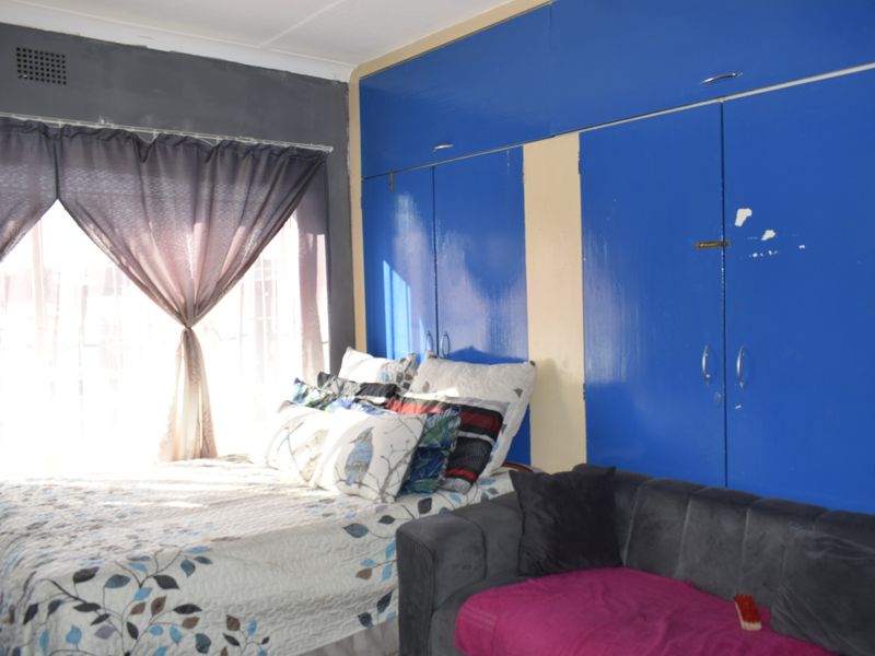 Bedroom featuring large built-in blue cupboards and natural light from a window. The room requires cosmetic updates to finishes and paintwork.