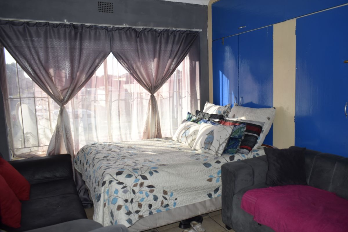 Bedroom featuring built-in cupboards, tiled flooring, and security bars on the window. The room requires cosmetic updates to improve its overall condition.
