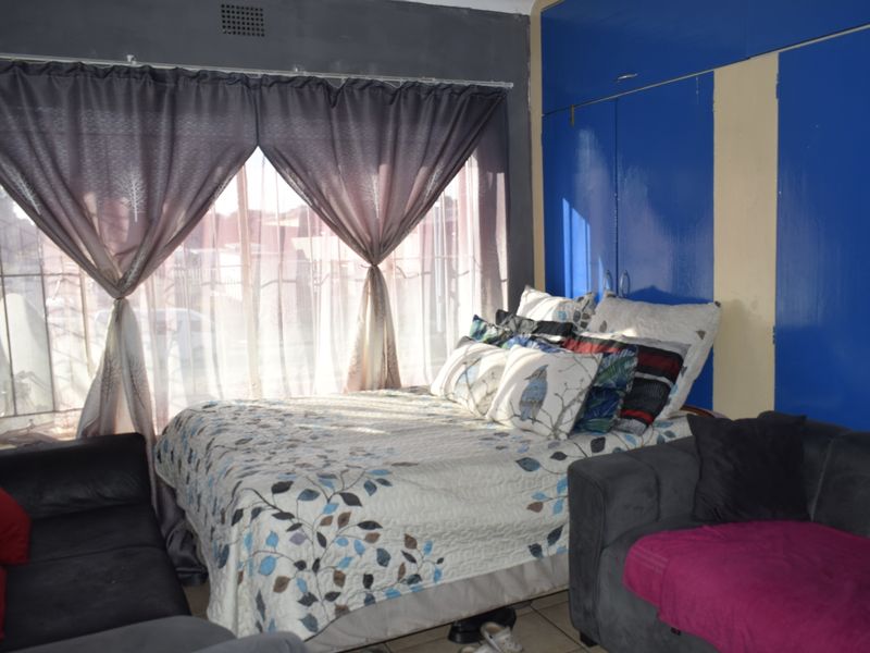 Bedroom featuring built-in cupboards, tiled flooring, and security bars on the window. The room requires cosmetic updates to improve its overall condition.