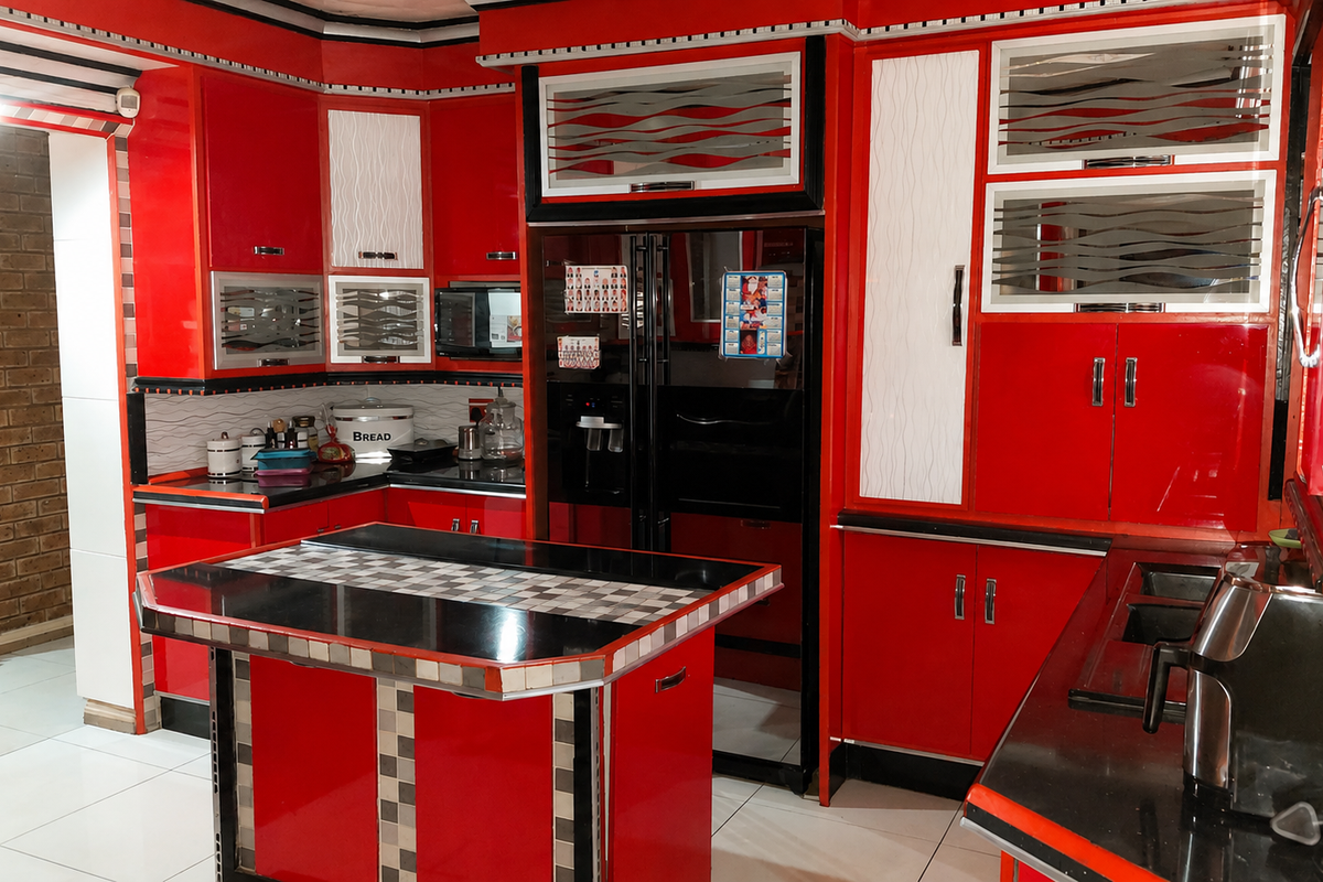 A vibrant kitchen featuring bold red cabinetry, a central island with a black countertop, and an exposed brick feature wall.