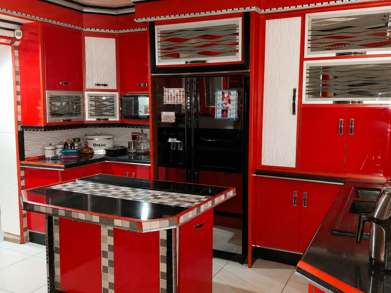 A vibrant kitchen featuring bold red cabinetry, a central island with a black countertop, and an exposed brick feature wall.