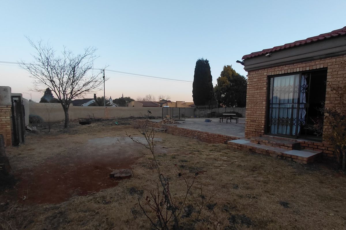 Rear view of the property featuring a brick facade, paved patio area, and a large backyard with boundary walling.