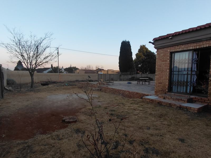Rear view of the property featuring a brick facade, paved patio area, and a large backyard with boundary walling.