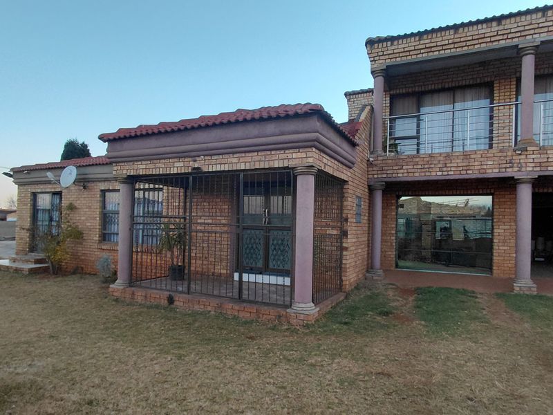 Rear view of a double-story face brick house featuring a ground-floor security-gated patio and an upper-level balcony with stainless steel balustrades.