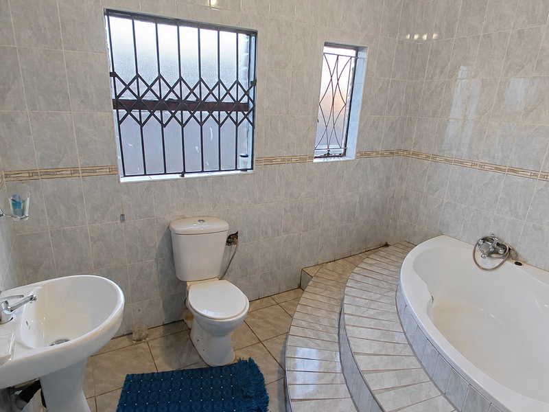 A functional bathroom featuring a pedestal basin, toilet, and a raised tiled platform with a built-in corner bathtub, finished with full-height wall tiling.