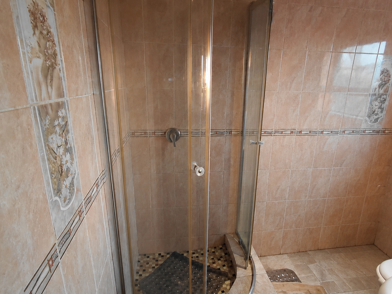 A dated bathroom featuring a corner shower enclosure with glass doors, ceramic wall tiling with decorative accents, and a standard toilet.