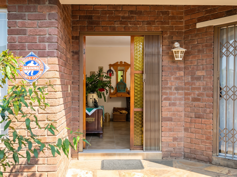 Front entrance featuring a brick facade, security gate, and sliding glass door leading into the home interior.