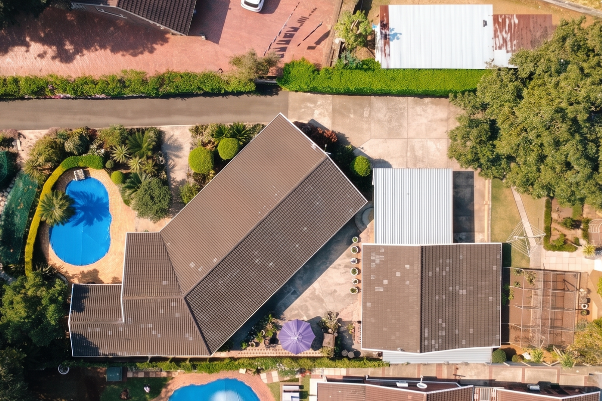 Aerial view of the property showcasing the main dwelling, swimming pool, paved driveway, and established garden areas on a spacious residential lot.