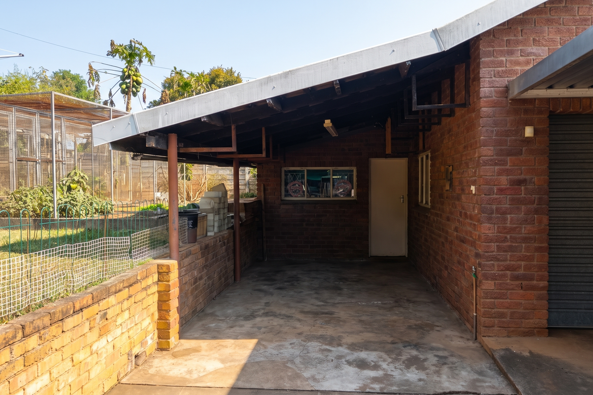 A covered rear patio area featuring exposed brick walls, a concrete floor, and direct access to the garage and garden space.