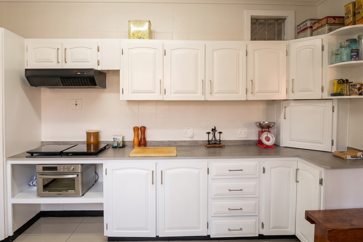 A clean, functional kitchen featuring white cabinetry, laminate countertops, a built-in electric hob, and a tiled backsplash.
