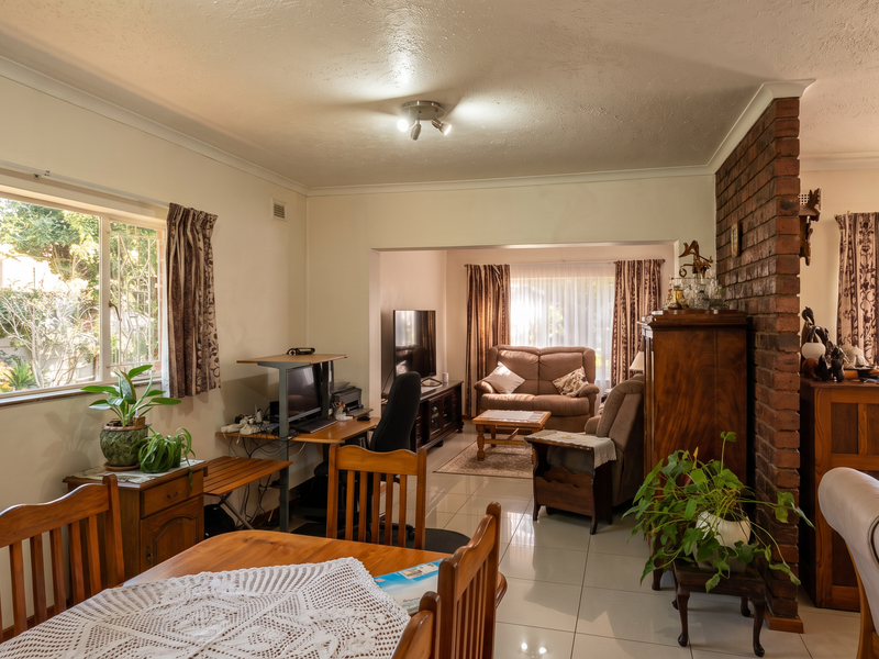 Spacious open-plan living and dining area featuring an exposed brick partition wall, large windows providing natural light, and neutral tiled flooring throughout.