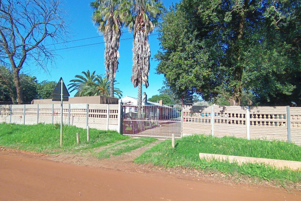 Street view of the property entrance featuring a precast concrete boundary wall and a metal driveway gate.