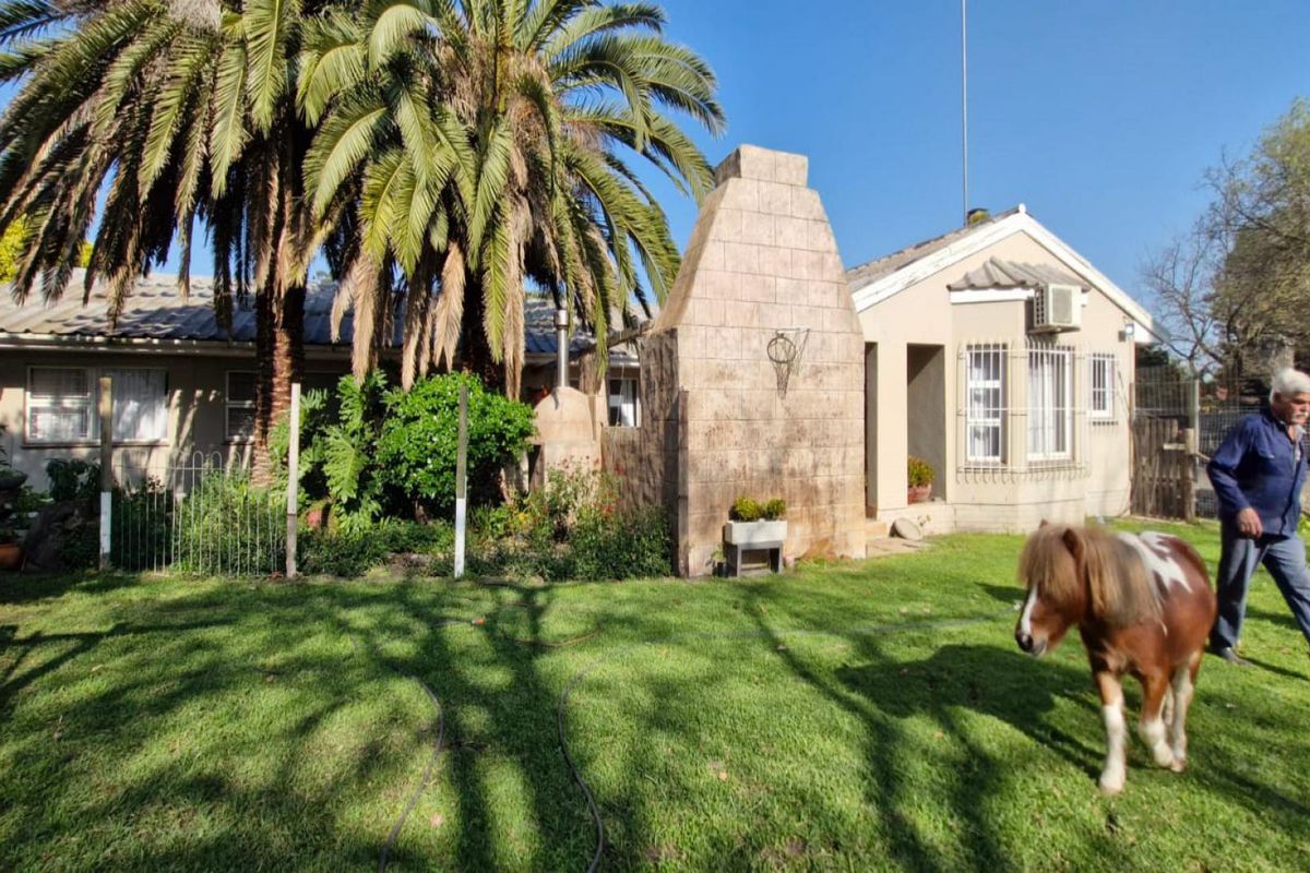 Rear view of the farm property featuring a large stone-clad outdoor fireplace, established garden, and security-fitted windows.