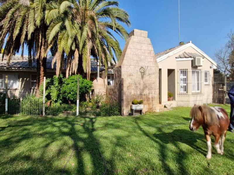 Rear view of the farm property featuring a large stone-clad outdoor fireplace, established garden, and security-fitted windows.