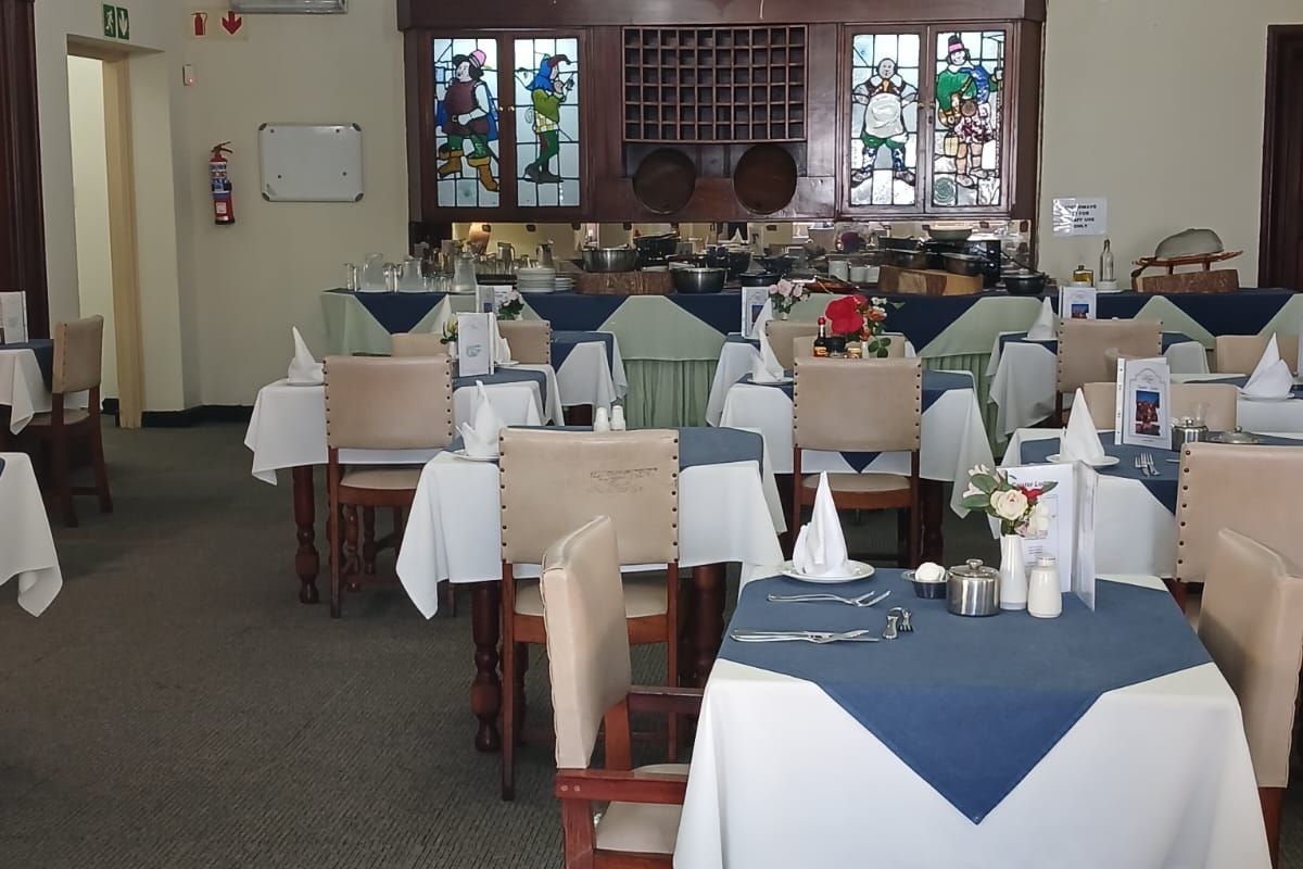 A spacious dining area featuring traditional timber ceiling beams, decorative chandeliers, and built-in stained glass cabinetry, suitable for a restaurant or communal dining setting.