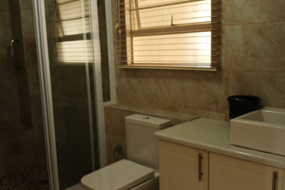 A functional bathroom featuring a shower enclosure, toilet, and a vanity cabinet with a vessel sink, finished with neutral wall and floor tiles.