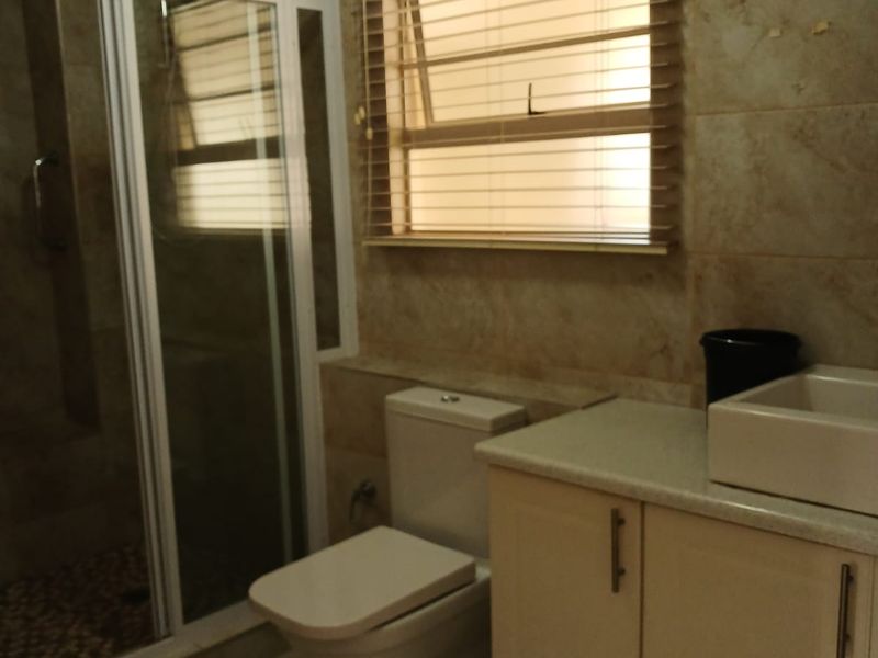 A functional bathroom featuring a shower enclosure, toilet, and a vanity cabinet with a vessel sink, finished with neutral wall and floor tiles.