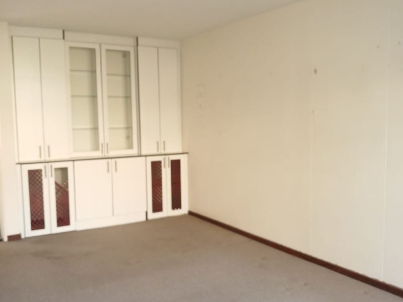 An empty living room featuring built-in white cabinetry, neutral carpet flooring, and a simple ceiling light fixture.