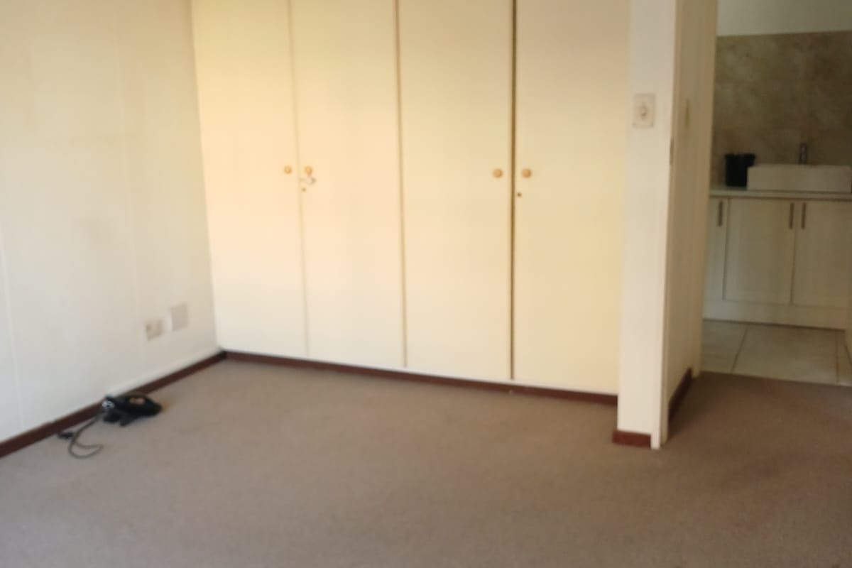 An empty bedroom featuring built-in cupboards and carpeted flooring, with an adjacent view into a bathroom area.