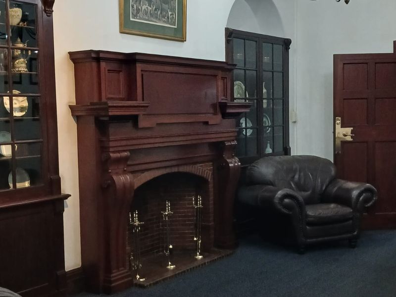 A traditional living room featuring a prominent timber fireplace mantel, built-in display cabinetry, recessed archways, and classic architectural detailing.