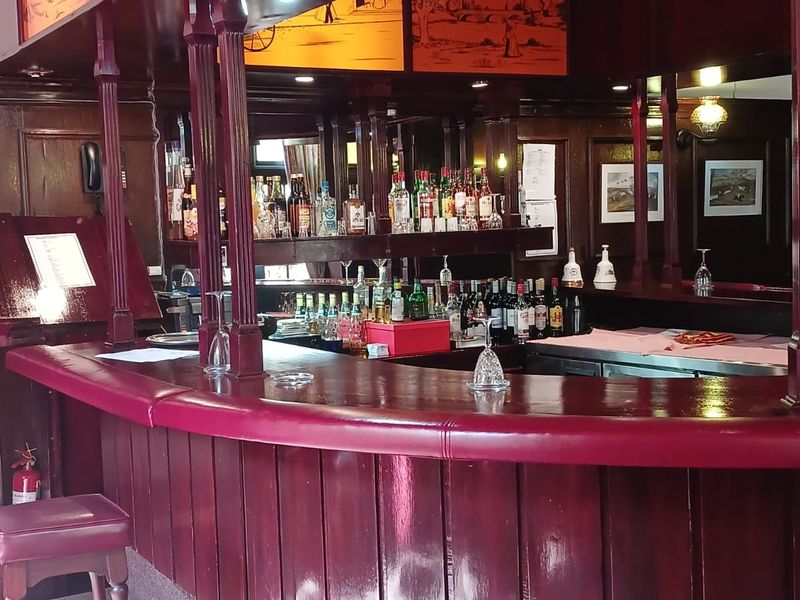 A traditional style built-in bar area featuring dark timber paneling, a curved counter, and integrated shelving for display.