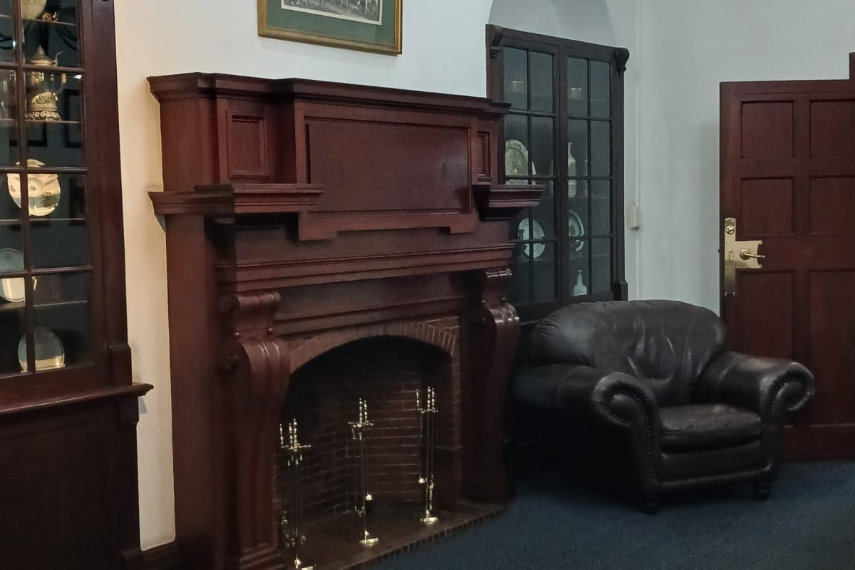 A traditional living room featuring a prominent timber fireplace, built-in display cabinetry, arched alcoves, and exposed timber ceiling beams.