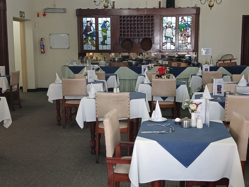 A spacious dining area featuring traditional timber ceiling beams, decorative chandeliers, and built-in stained glass cabinetry, suitable for a restaurant or communal dining setting.
