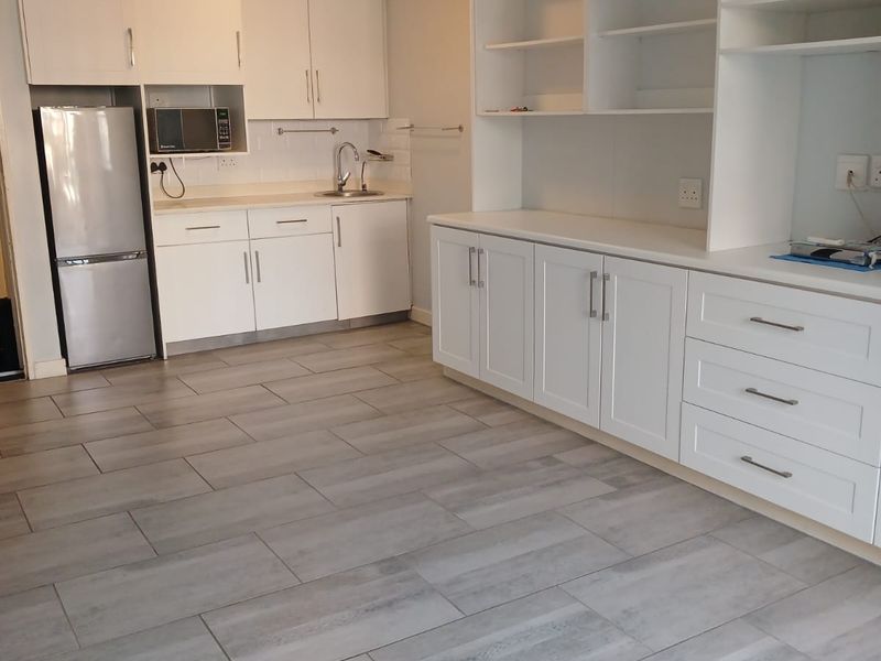A clean, modern kitchen featuring white built-in cabinetry, extensive shelving, tiled flooring, and a ceiling fan in an open-plan layout.