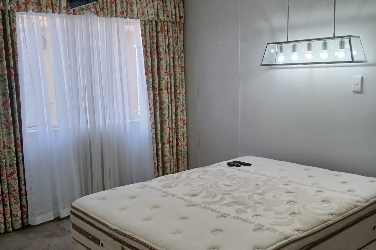 A bedroom featuring carpeted flooring, a ceiling-mounted television bracket, and a modern pendant light fixture, providing a functional space for rest.