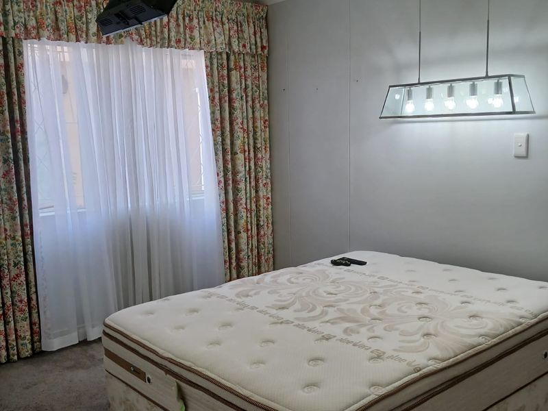 A bedroom featuring carpeted flooring, a ceiling-mounted television bracket, and a modern pendant light fixture, providing a functional space for rest.