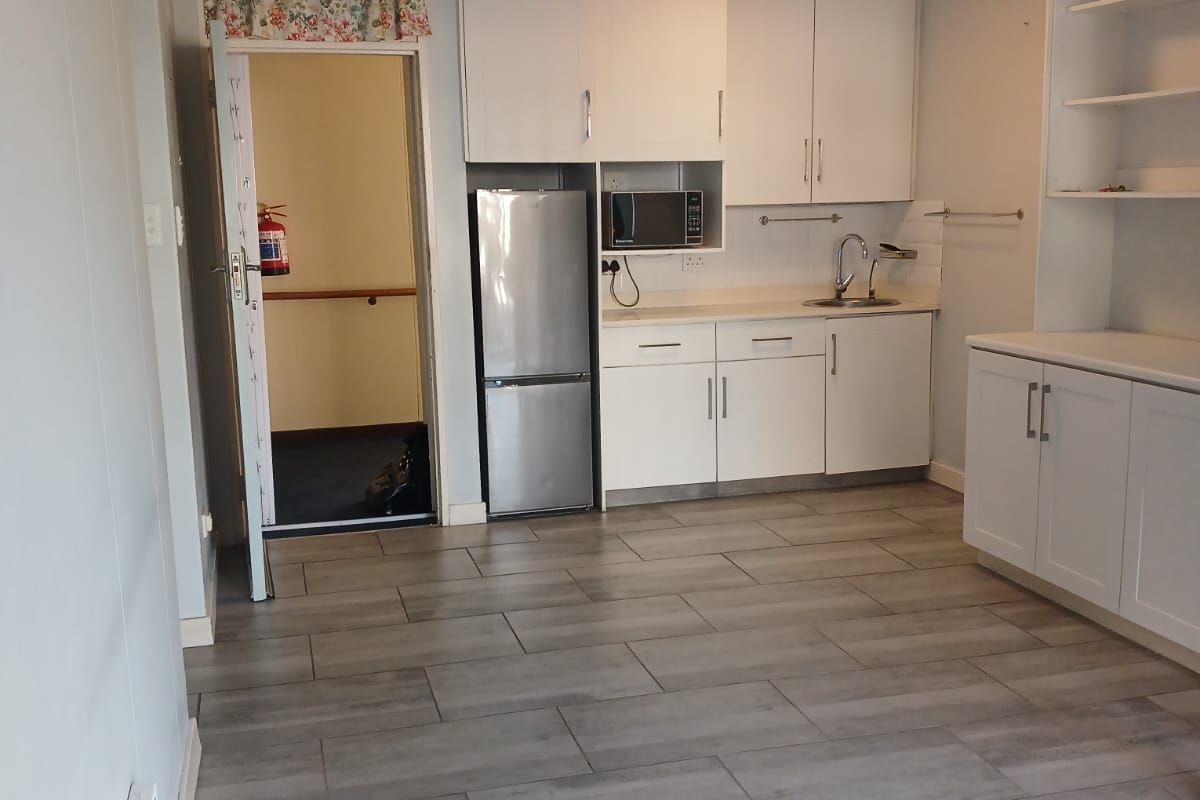 A functional kitchen area featuring white built-in cabinetry, a stainless steel sink, built-in microwave, and modern grey tiled flooring.