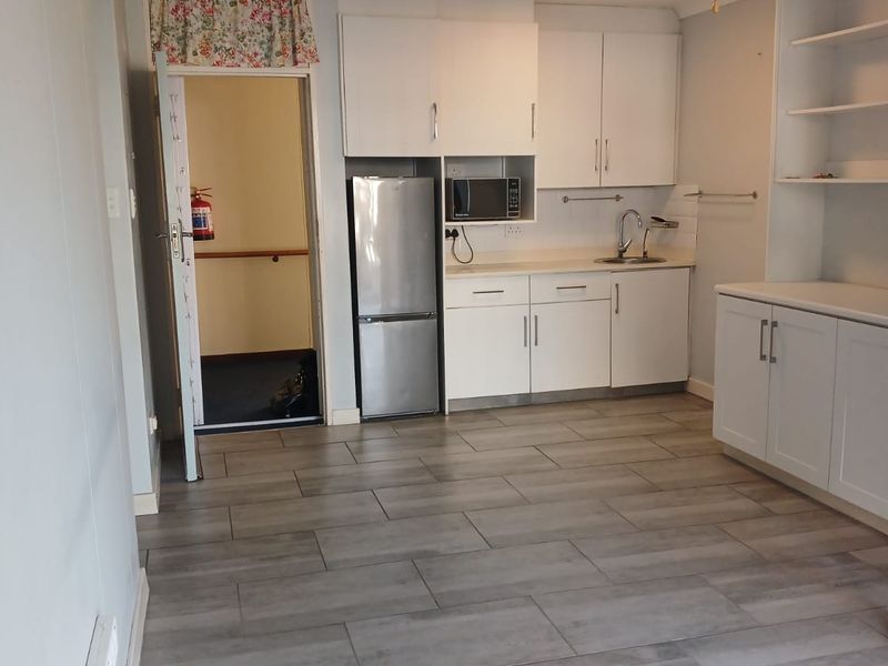 A functional kitchen area featuring white built-in cabinetry, a stainless steel sink, built-in microwave, and modern grey tiled flooring.