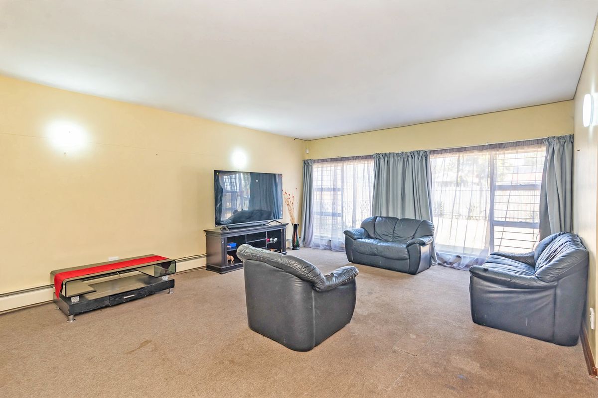 A spacious living room featuring large windows with curtain tracks and wall-mounted lighting, currently finished with wall-to-wall carpeting.