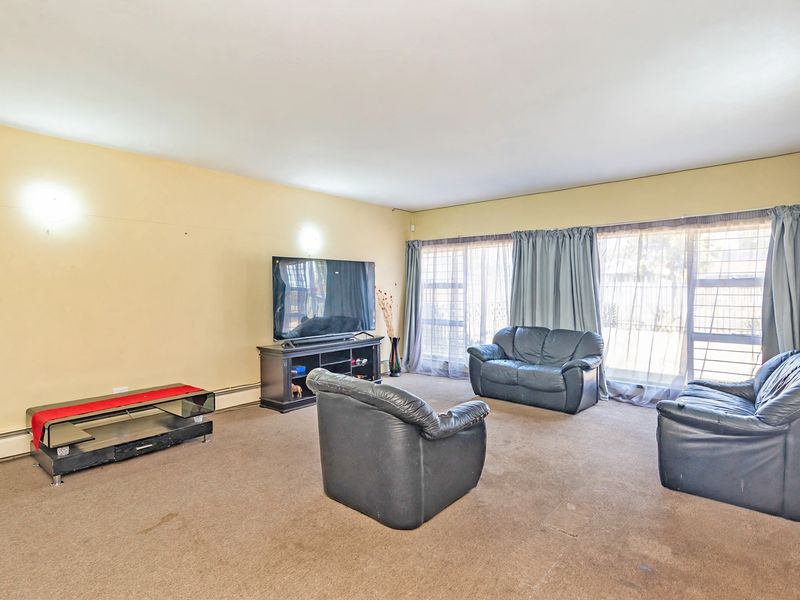 A spacious living room featuring large windows with curtain tracks and wall-mounted lighting, currently finished with wall-to-wall carpeting.
