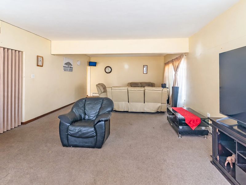 Spacious living room featuring neutral wall tones, carpeted flooring, and a folding door entrance, offering a functional layout for comfortable family living.