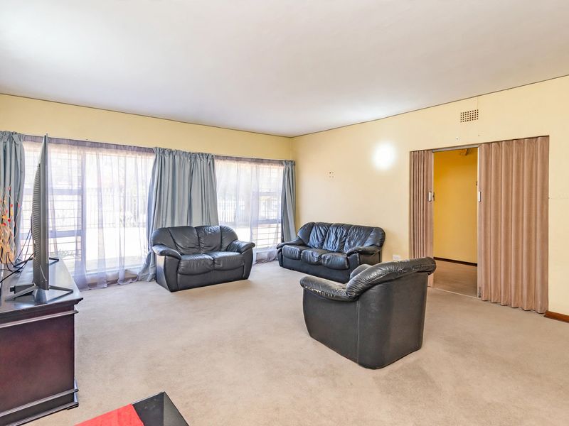 A spacious living room featuring large windows, carpeted flooring, and a sliding folding door leading to an adjacent room.