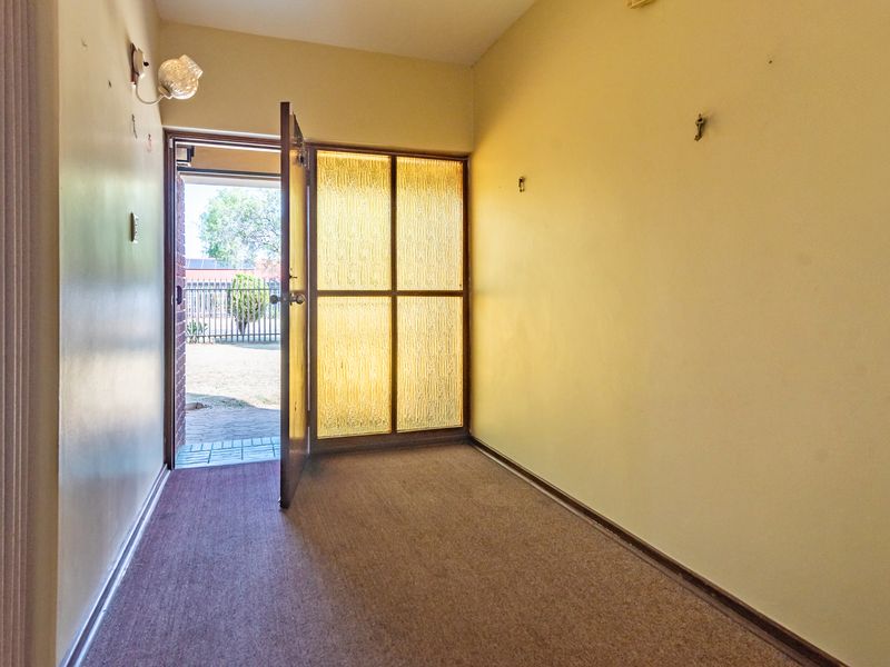 An empty entrance hall featuring carpeted flooring, a textured glass sidelight, and a wall-mounted light fixture.