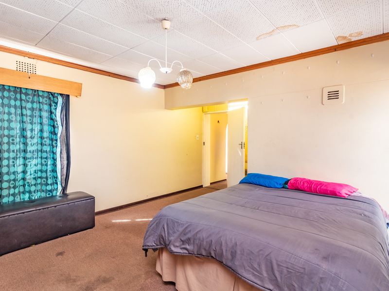 A bedroom featuring acoustic ceiling tiles with visible water staining, timber cornicing, and carpeted flooring.
