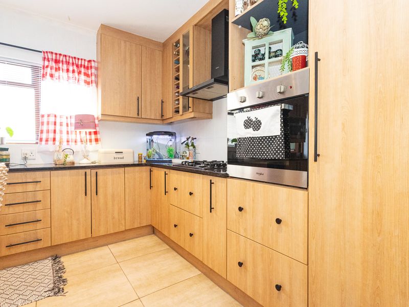 A functional kitchen featuring light wood-toned cabinetry, dark countertops, a built-in oven, gas hob, and tiled flooring.