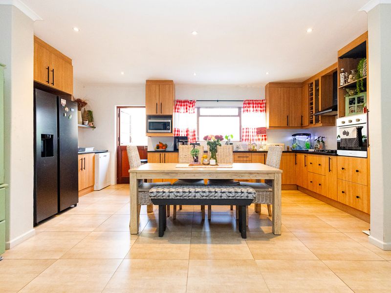 Spacious open-plan kitchen and dining area featuring warm-toned wooden cabinetry, tiled flooring, and integrated appliances, offering a functional and inviting layout.