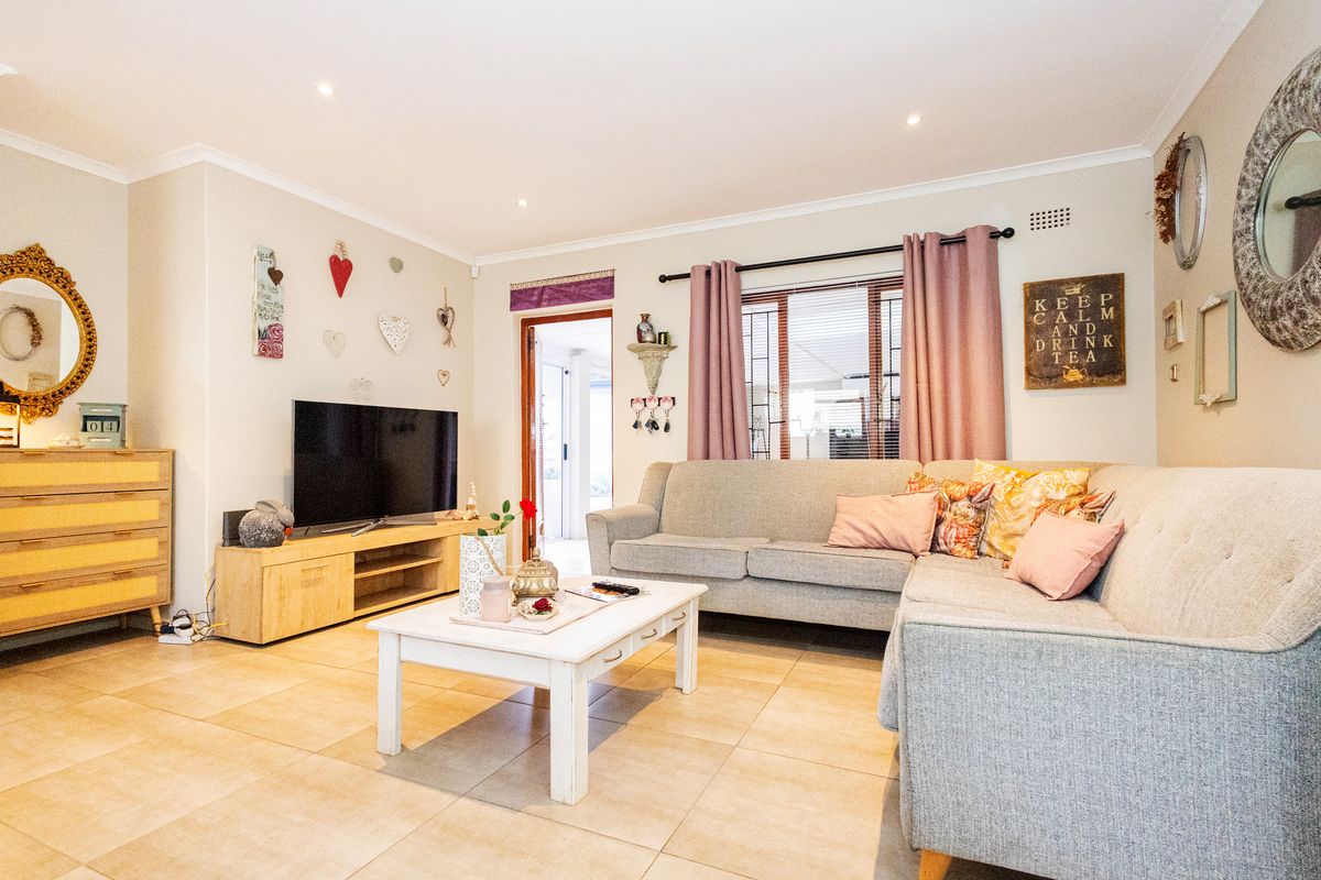 A comfortable living room featuring tiled flooring, recessed downlighting, and a window with security bars, offering a functional and well-maintained space.