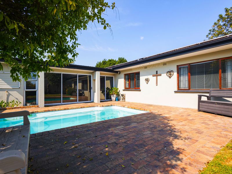 A well-maintained outdoor pool area featuring brick paving, sliding door access to the home, and secure aluminium-framed windows.