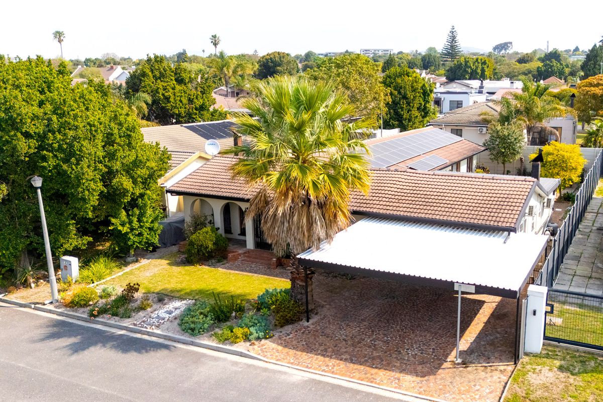 Aerial view of a residential property featuring a tiled roof with solar panels, a paved driveway, and a covered carport.