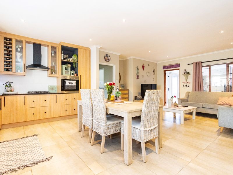 Spacious open-plan living area featuring a modern kitchen with light wood cabinetry, integrated appliances, and tiled flooring throughout the dining and lounge space.