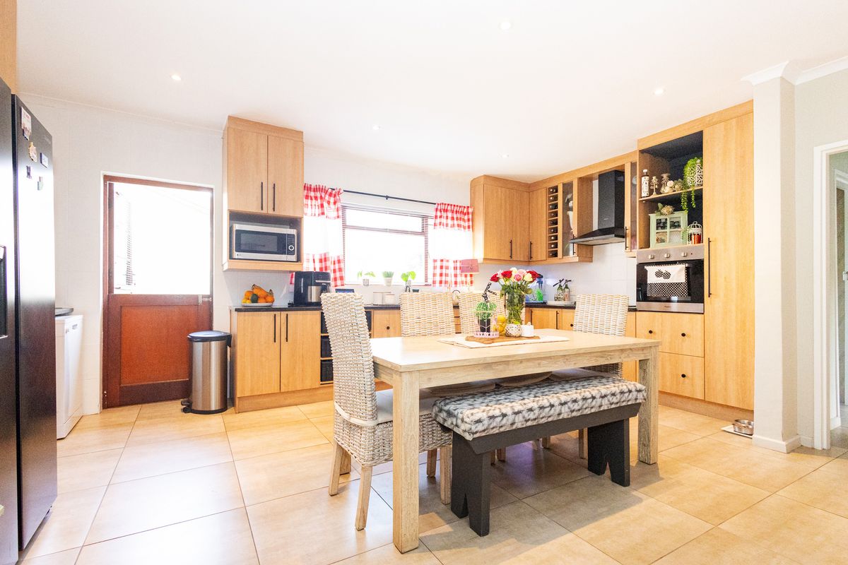 A functional kitchen featuring light wood cabinetry, built-in oven, extractor fan, and tiled flooring, with an integrated dining area.