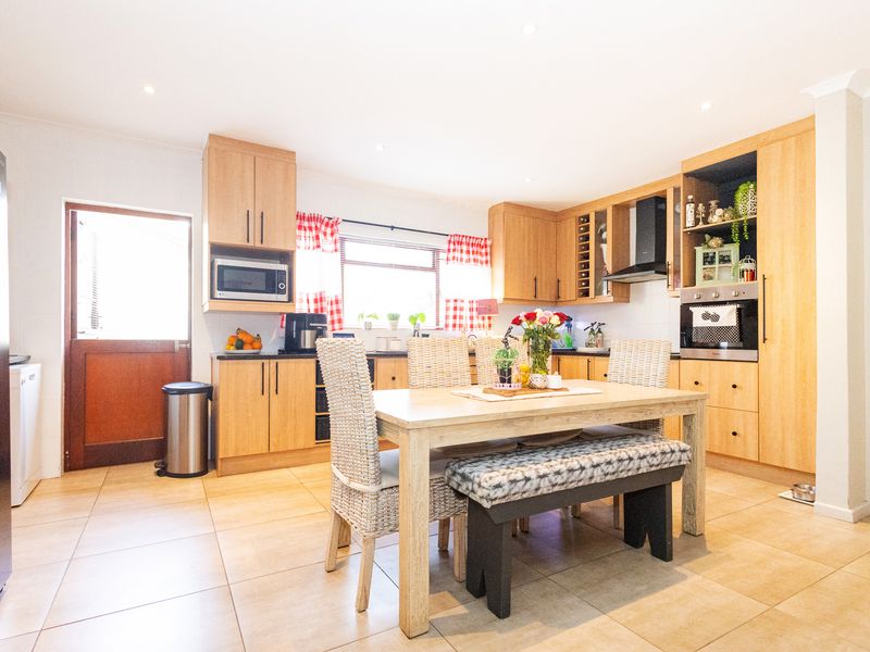 A functional kitchen featuring light wood cabinetry, built-in oven, extractor fan, and tiled flooring, with an integrated dining area.
